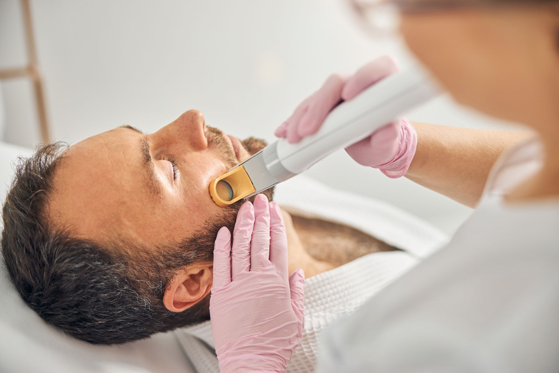 Laser facial treatment on a man lying back, with a clinician wearing pink gloves