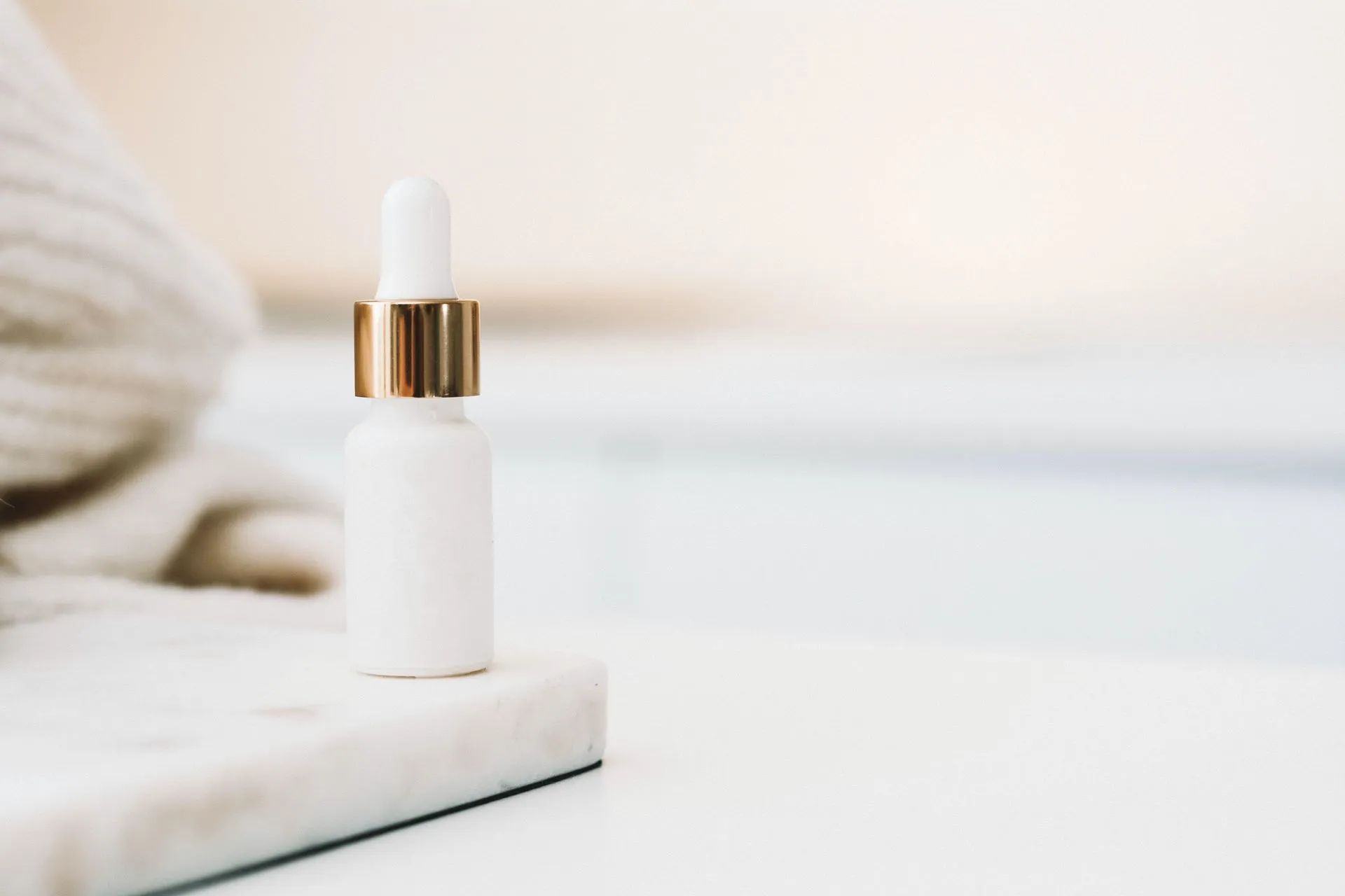 White skincare bottle with gold accents on marble block.