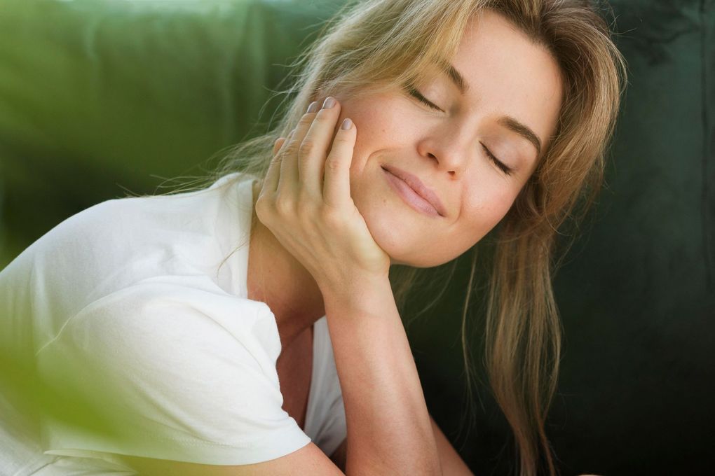 A woman is touching her face with her hands and looking up at the sky.