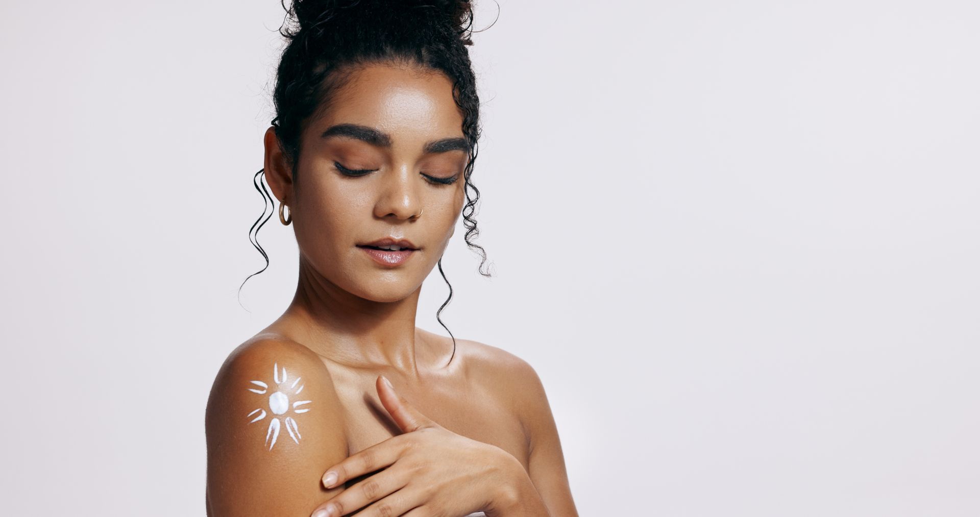 A person with a sun-shaped mark of white cream on their shoulder, looking down while touching their shoulder.