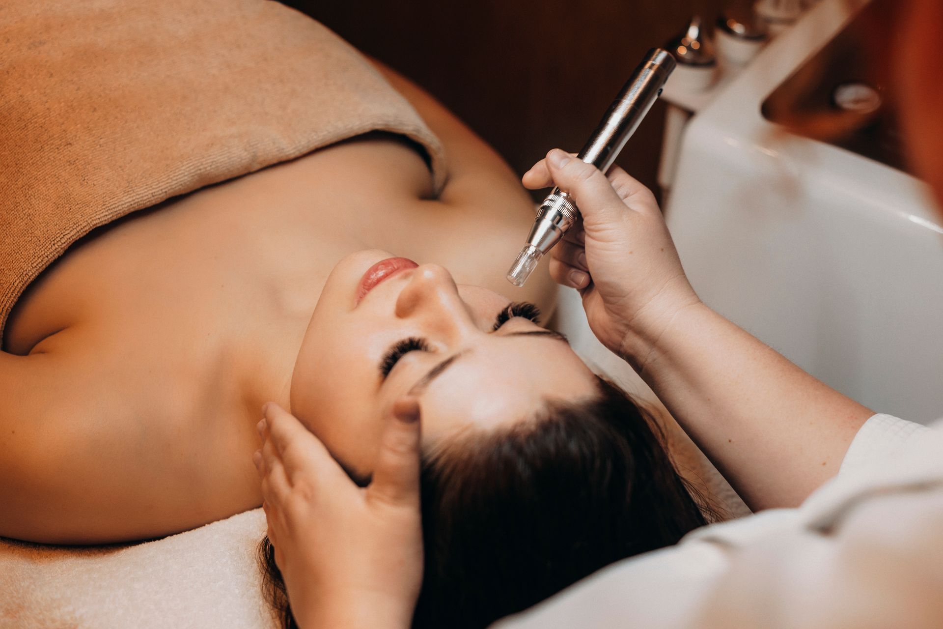 Woman receiving a facial treatment with a handheld beauty device on a spa bed