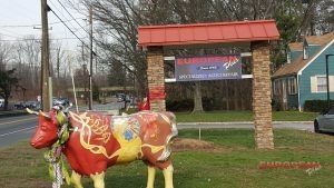 Colorful cow statue in front of a restaurant sign, next to a blue house. | European Plus