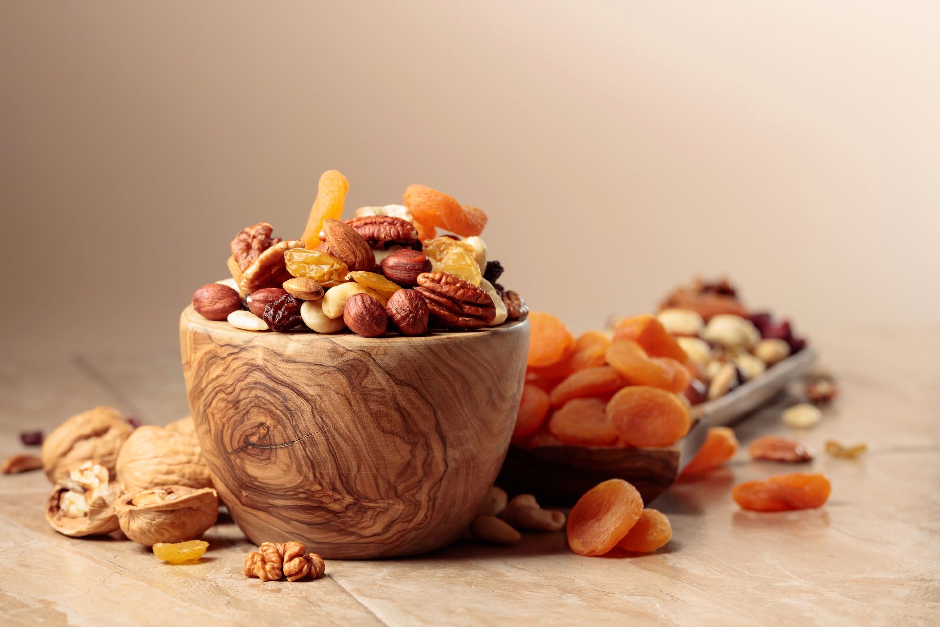 Una ciotola di legno con frutta secca mista e noci su un tavolo rustico, con altra frutta sparsa sullo sfondo.