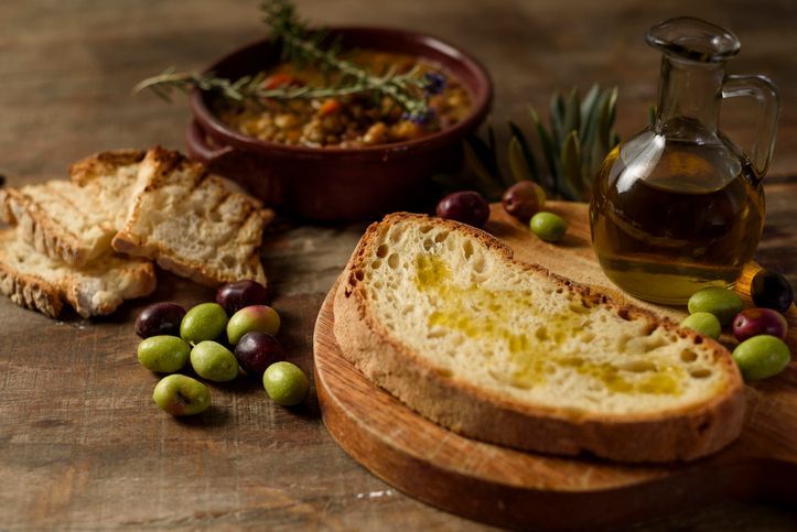 Tavolo rustico con pane, olive, hummus e bottiglia di olio d'oliva.