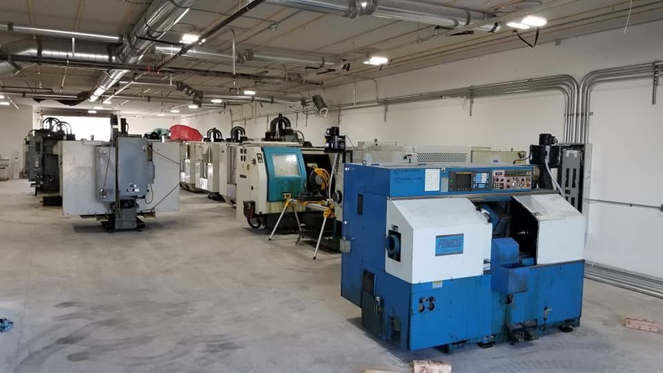Industrial workshop with large blue and gray machines lined up under fluorescent lights
