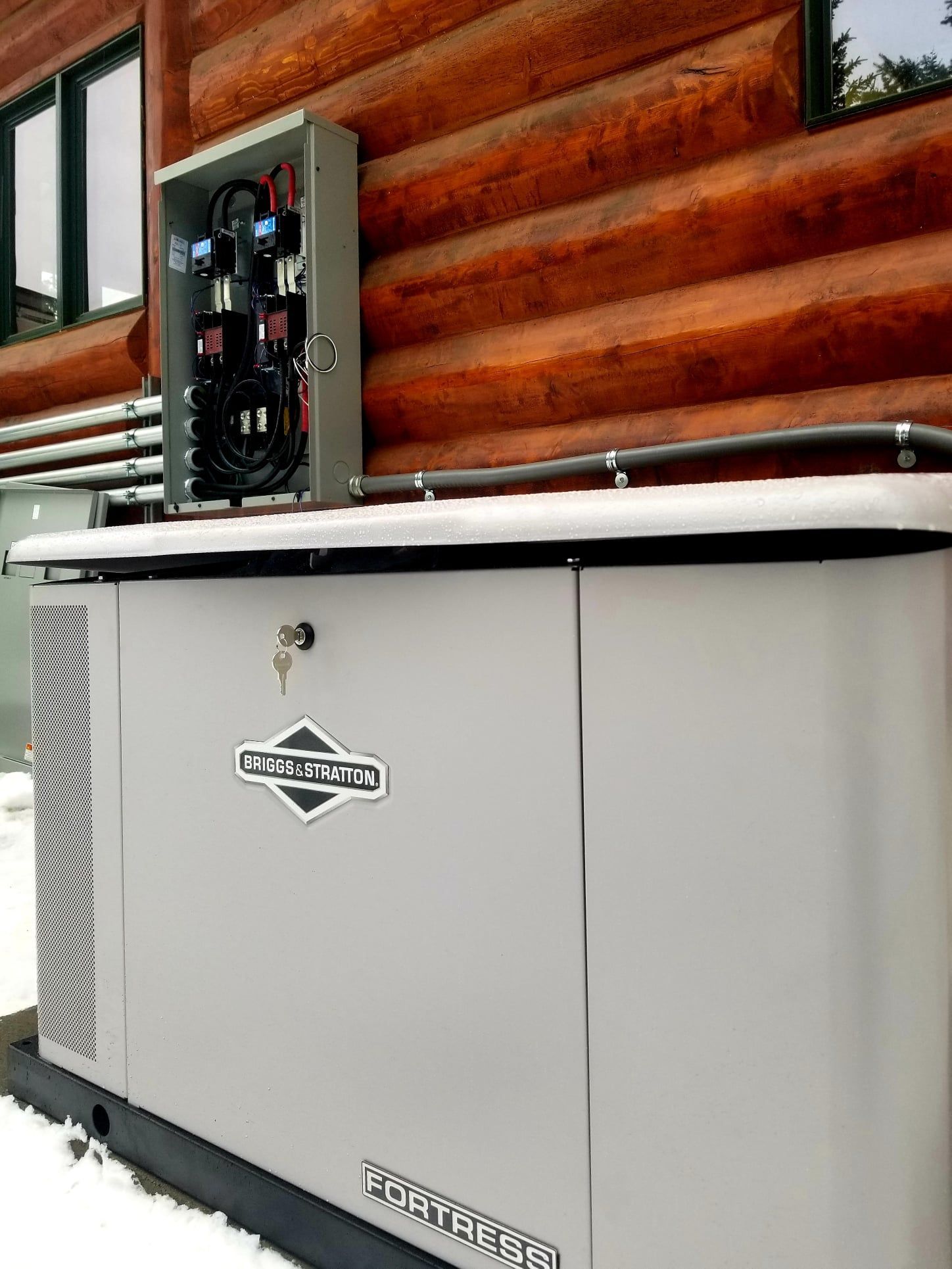 Outdoor generator beside a log cabin wall with an open electrical panel on top