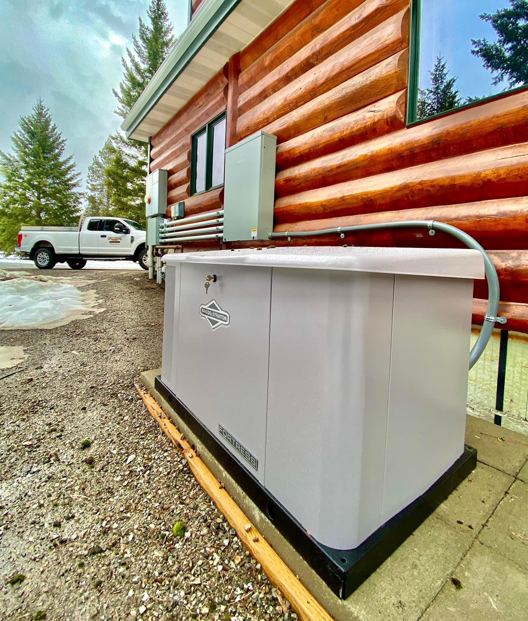 Outdoor hot tub beside a log cabin with a white pickup truck in the gravel driveway.