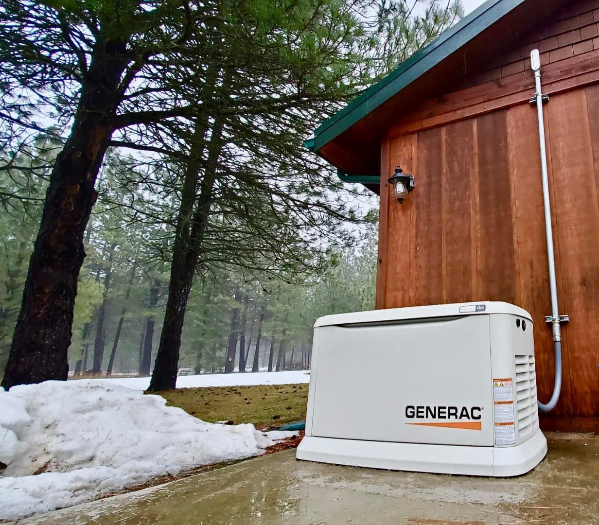 White Generac generator beside a wooden cabin in a snowy, wooded yard