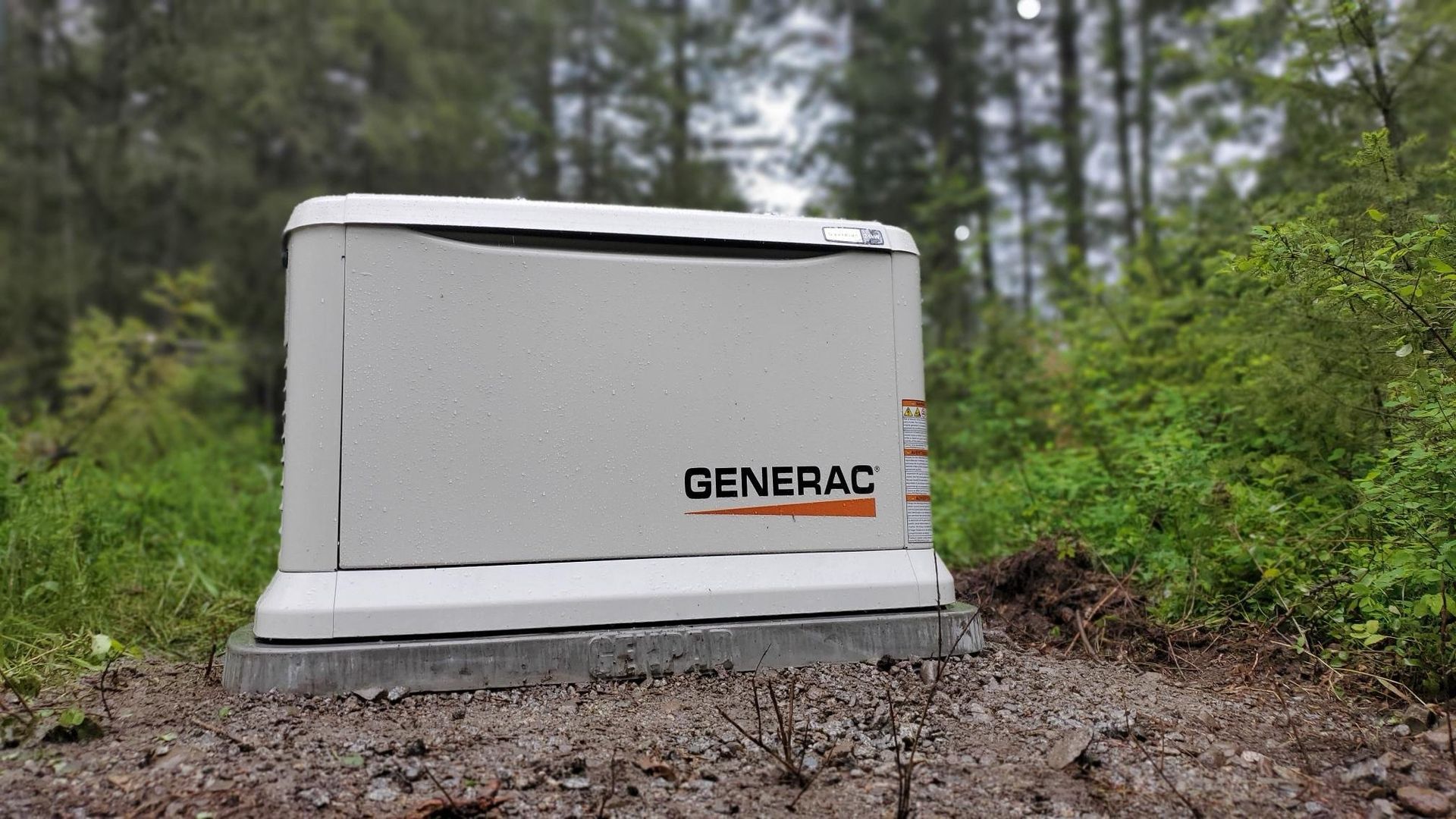 White Generac backup generator on gravel beside green trees and bushes outdoors