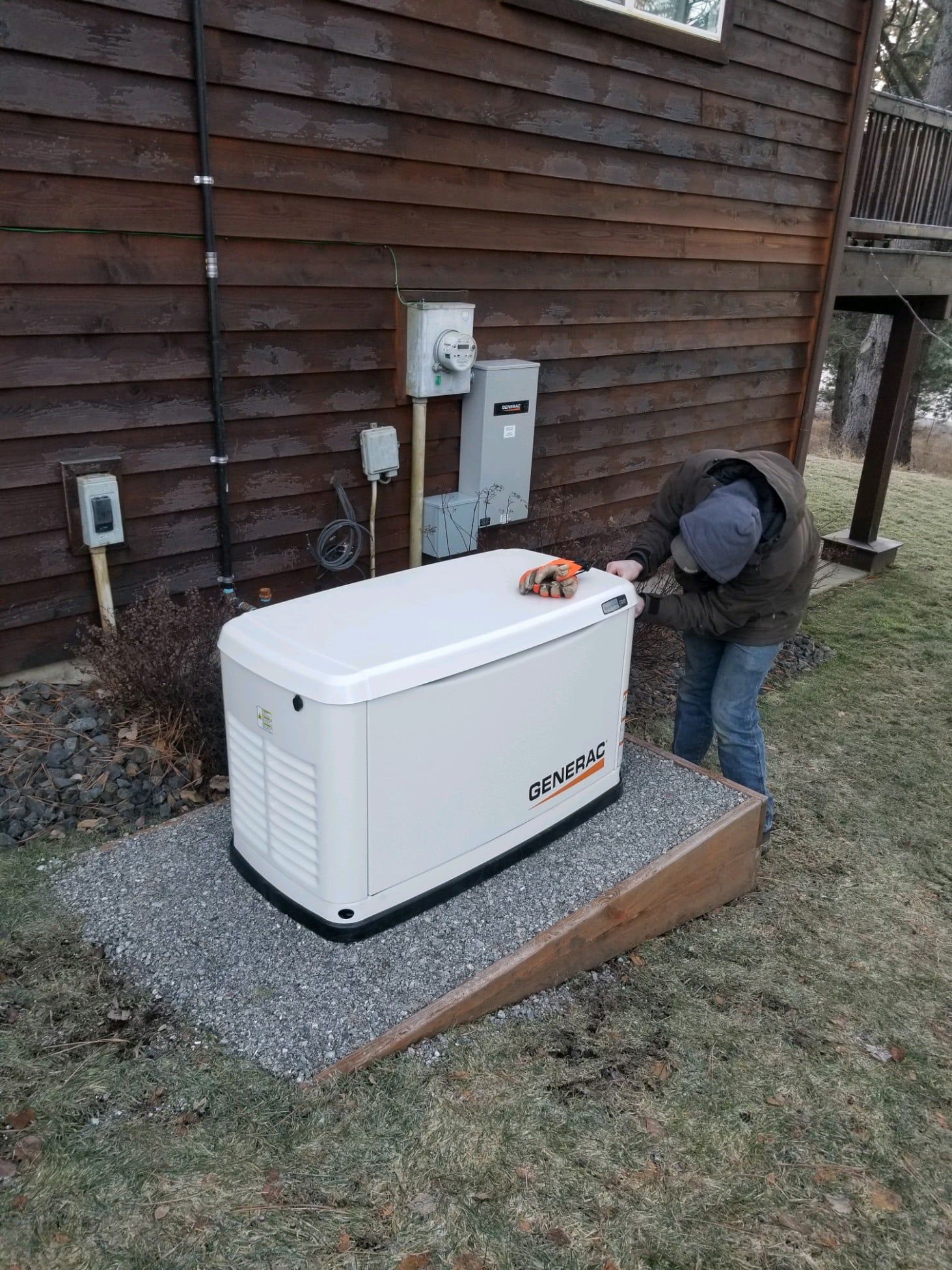 Technician inspecting a white backup generator beside a house exterior
