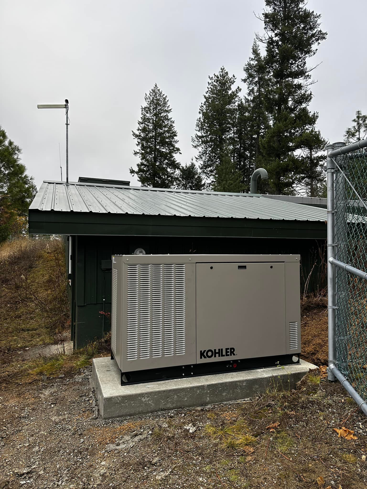 Outdoor Kohler generator beside a small green shed with a metal roof and gravel ground