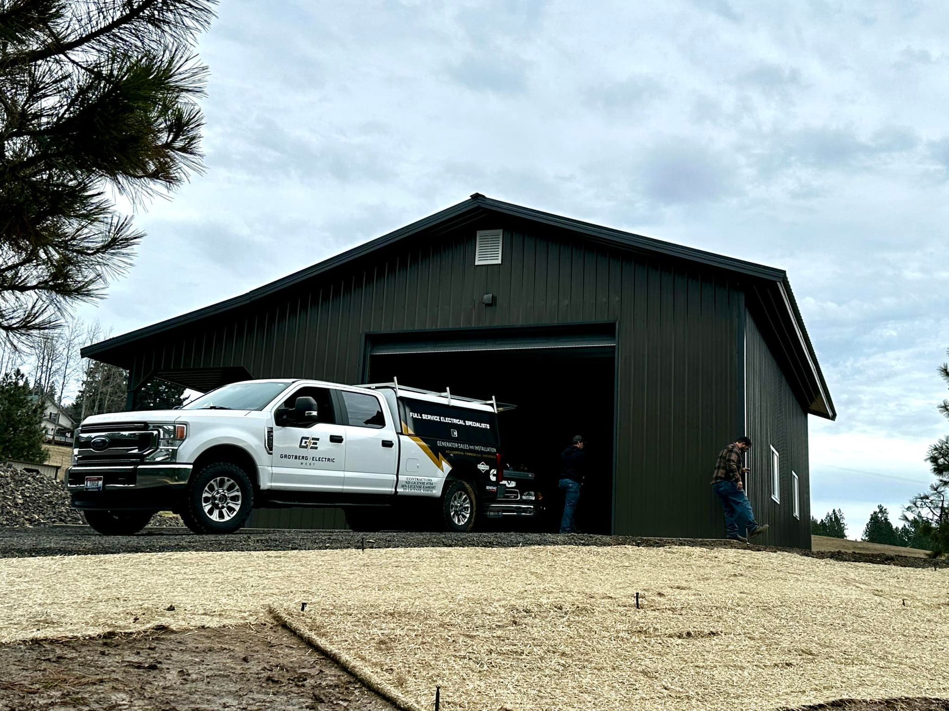 White work truck parked outside a dark green garage with a person standing near the open bay.