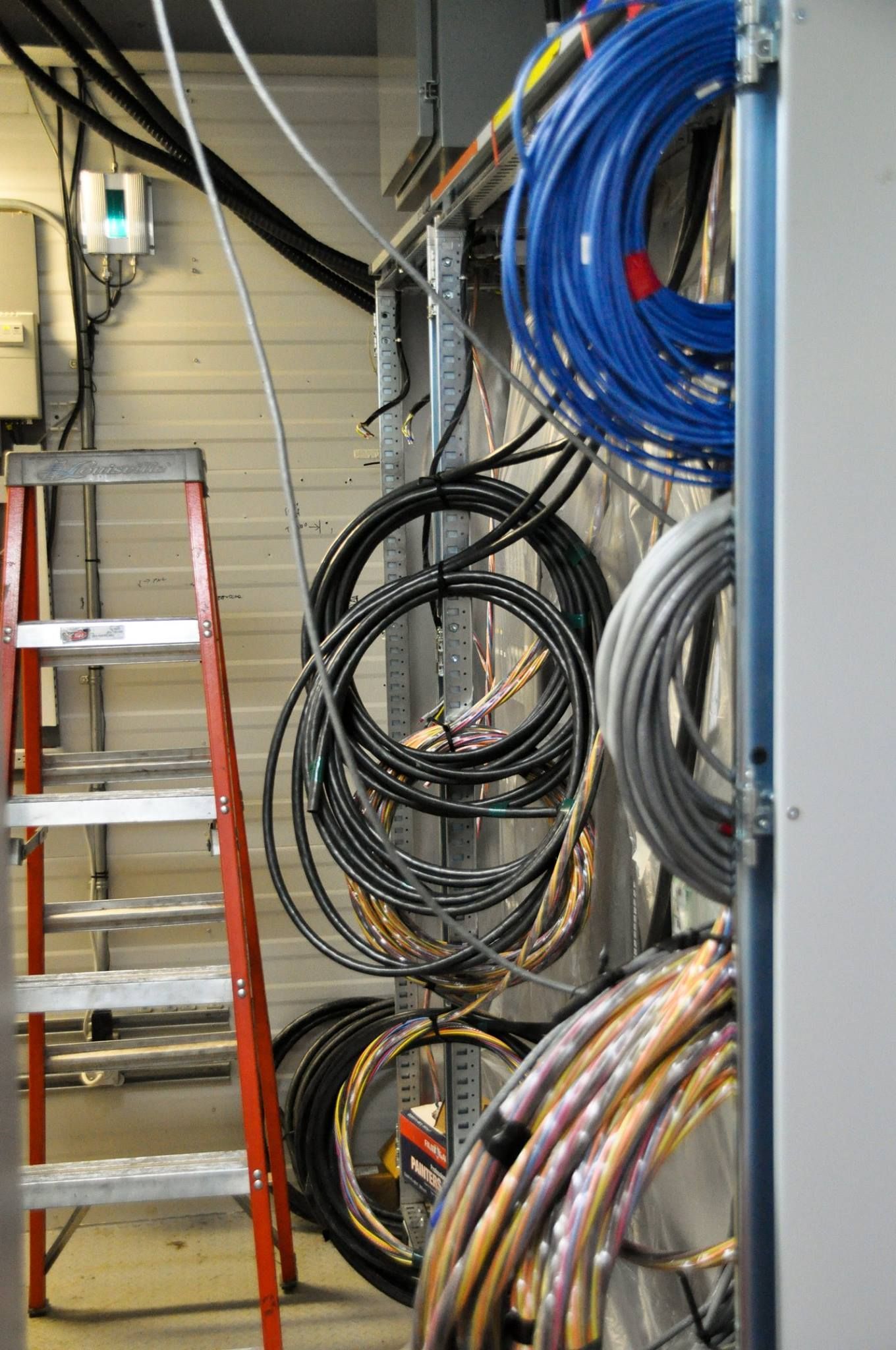 Coiled blue, black, and gray cables hanging in a utility room beside a red ladder