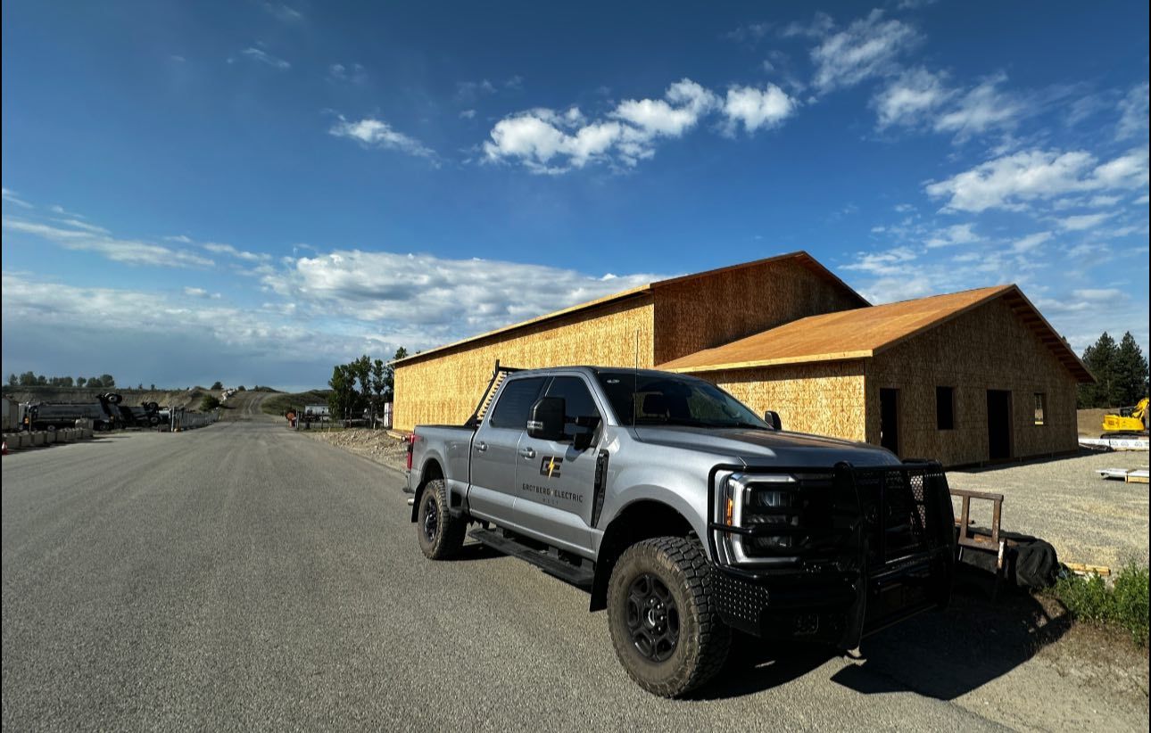 Black pickup truck parked beside a large wooden building under a blue sky with clouds.