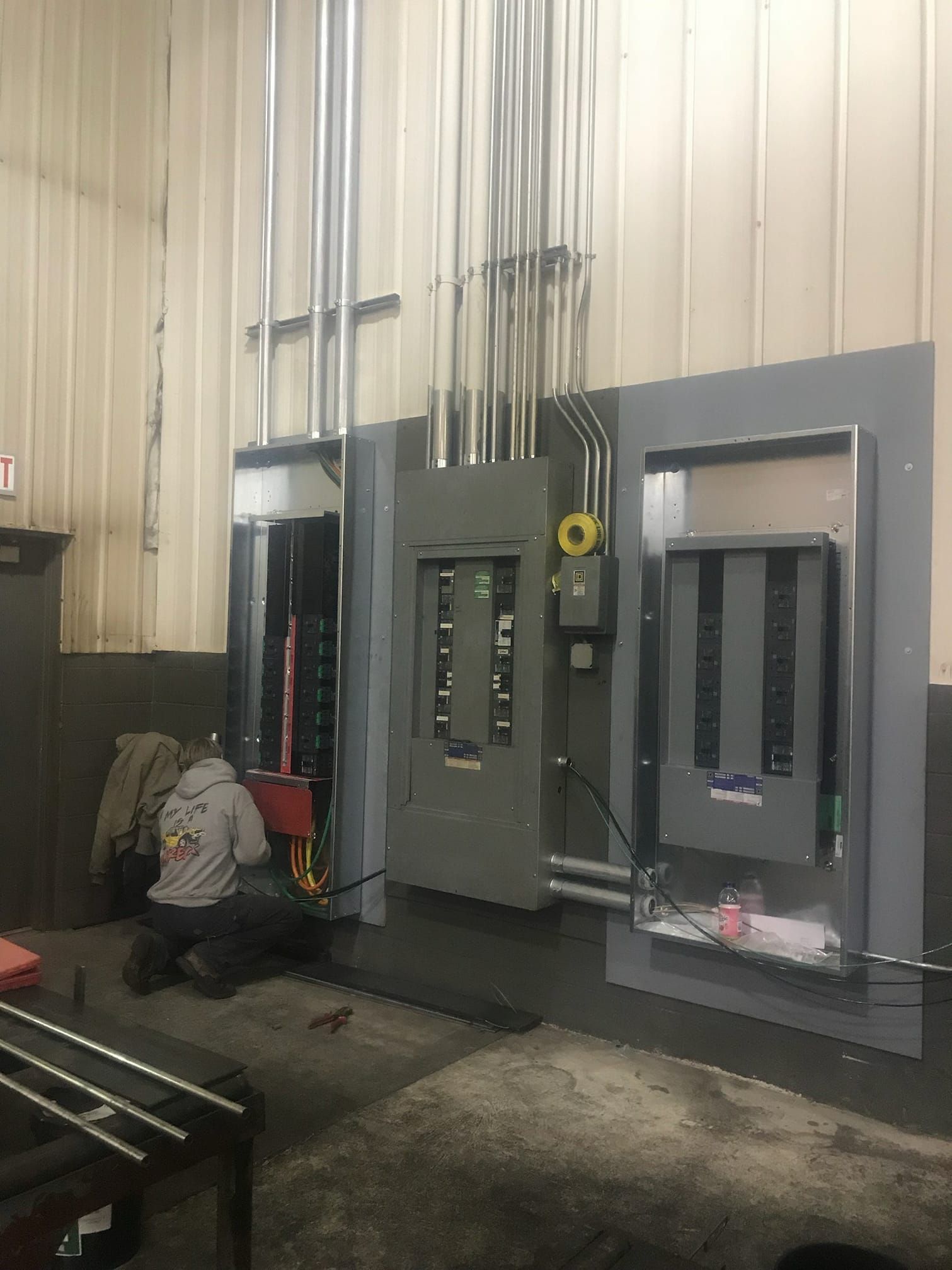 Worker kneels beside large industrial electrical panels in a workshop area
