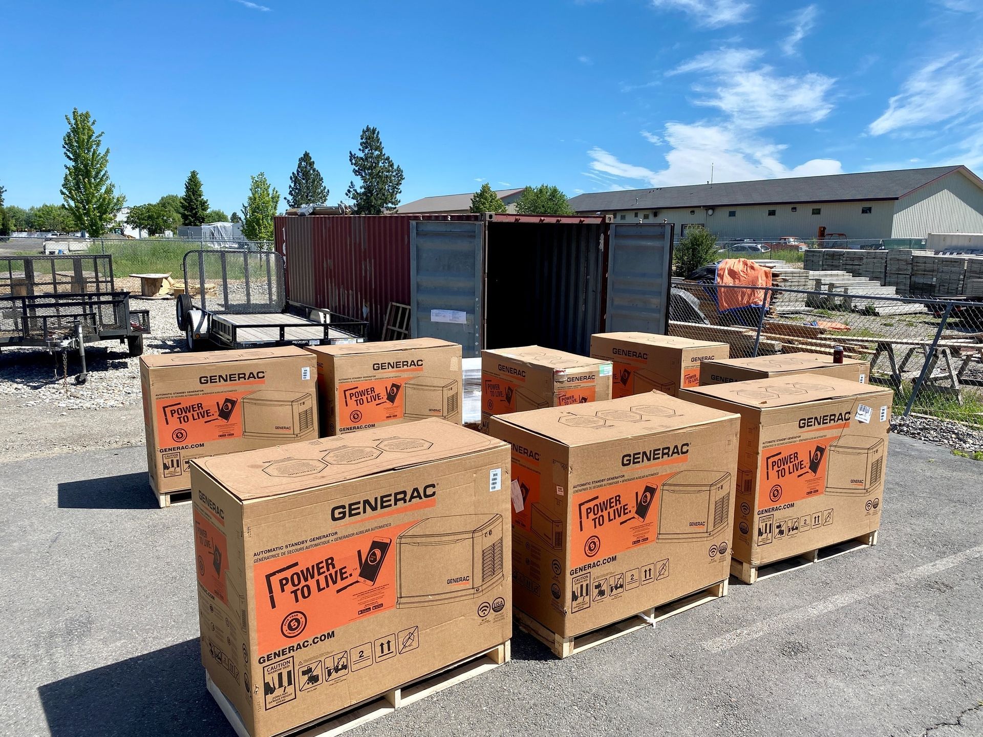 Stacked cardboard boxes in a yard beside shipping containers and construction equipment under a blue sky
