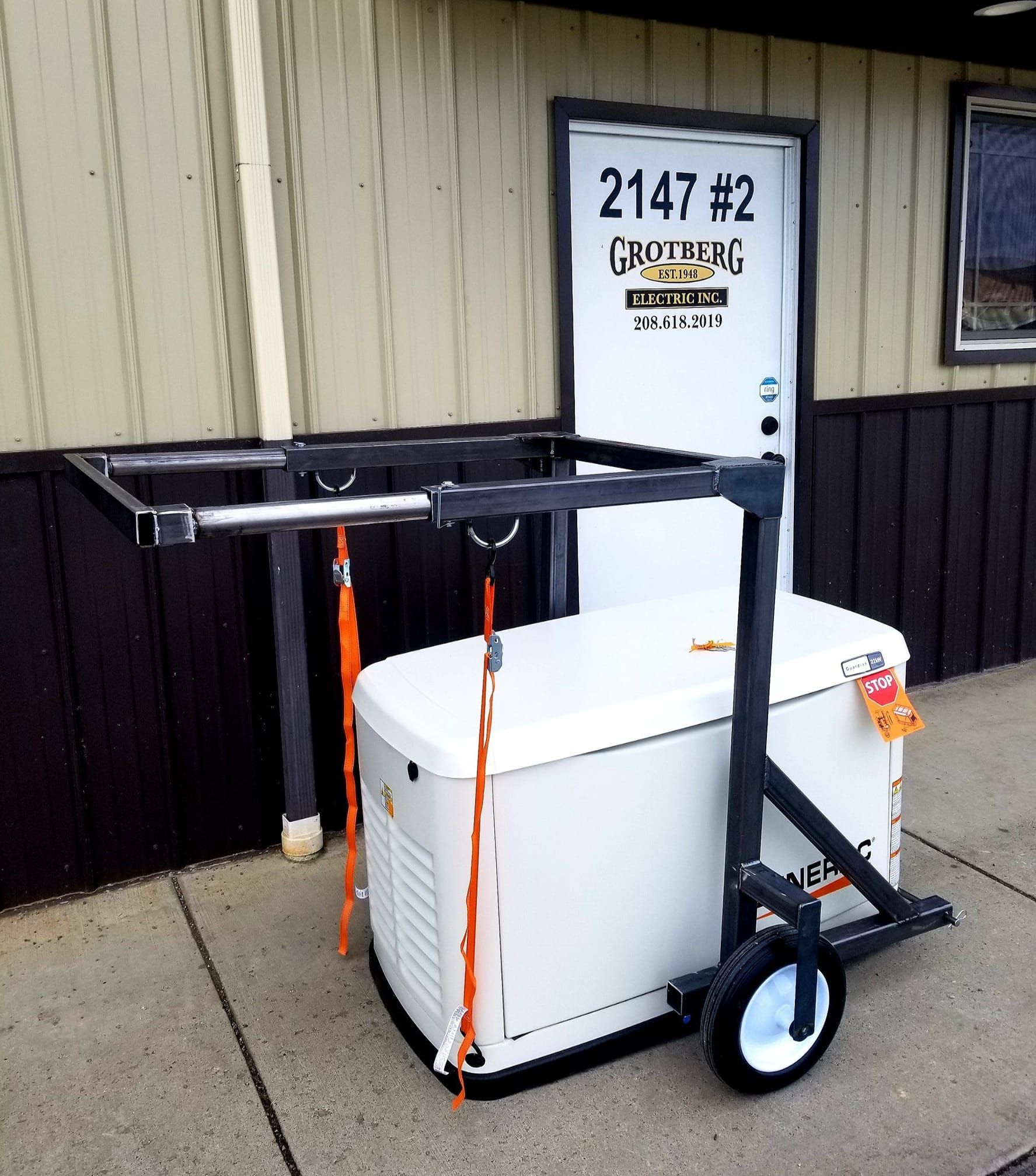 Black utility cart with a white cooler strapped on in front of a beige building door.