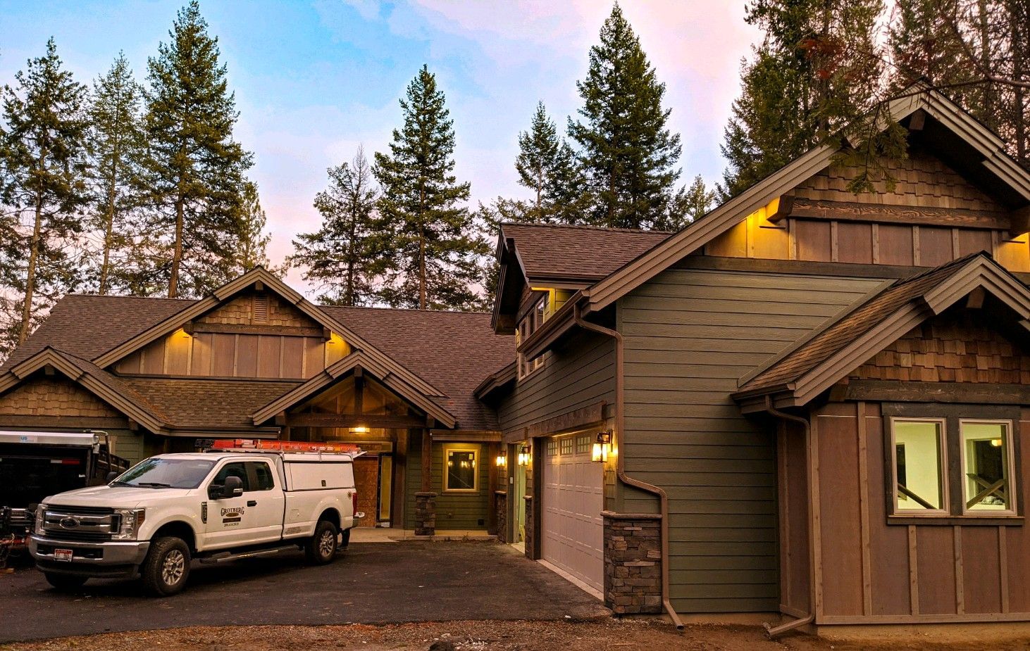 Lodge-style cabin at dusk with a white pickup truck parked outside, surrounded by tall pine trees.