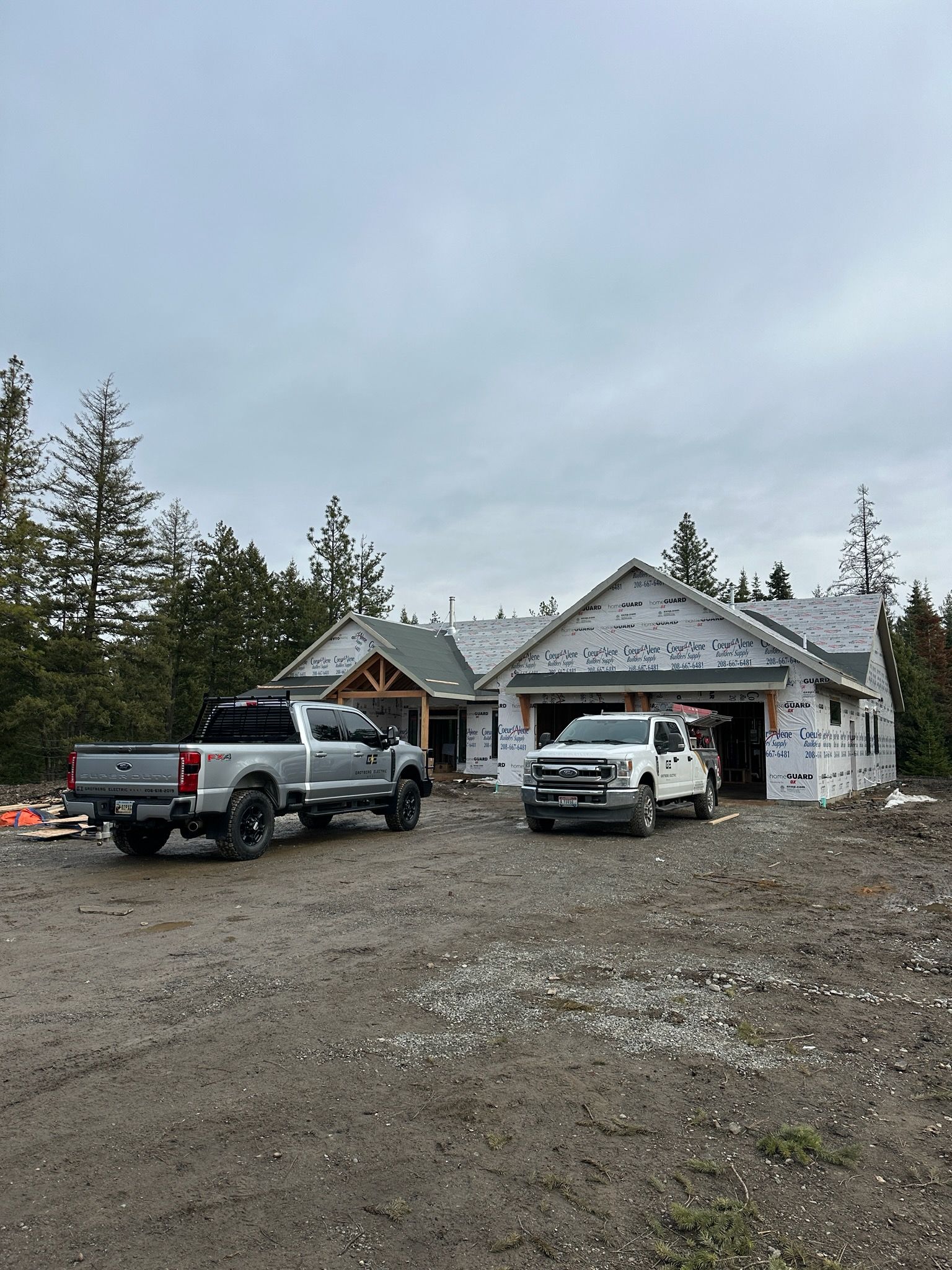 Two pickup trucks parked outside a partially built house on a muddy rural lot