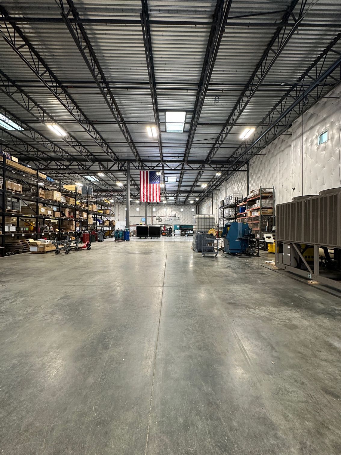 Large warehouse interior with tall shelving, polished concrete floor, and an American flag hanging at the far end.