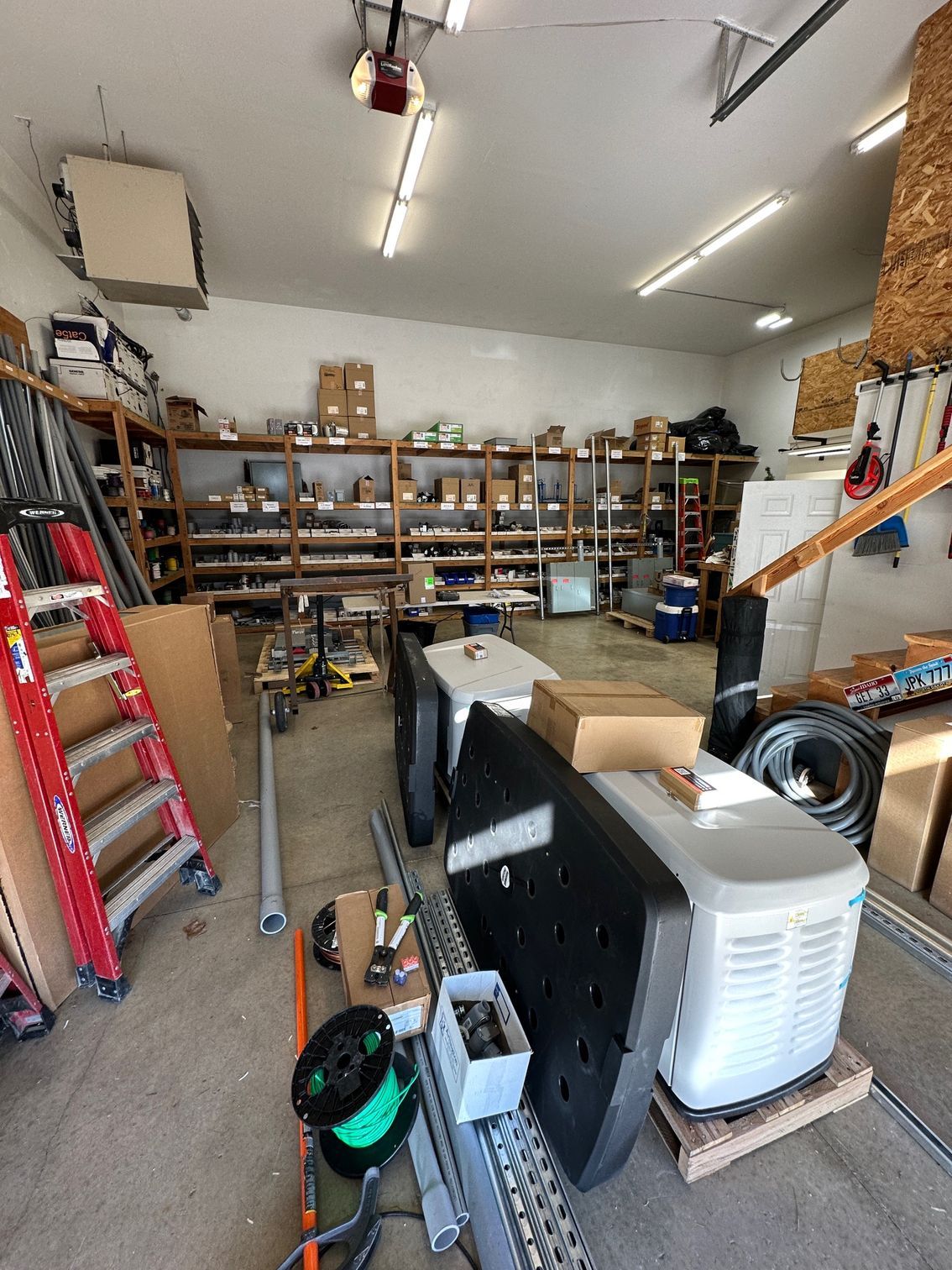 Cluttered workshop with shelves of tools, cardboard boxes, and a large machine in the foreground.