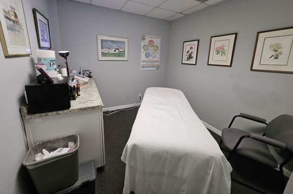 Examination room with red-covered table, gray walls, artwork, and a desk with a computer.