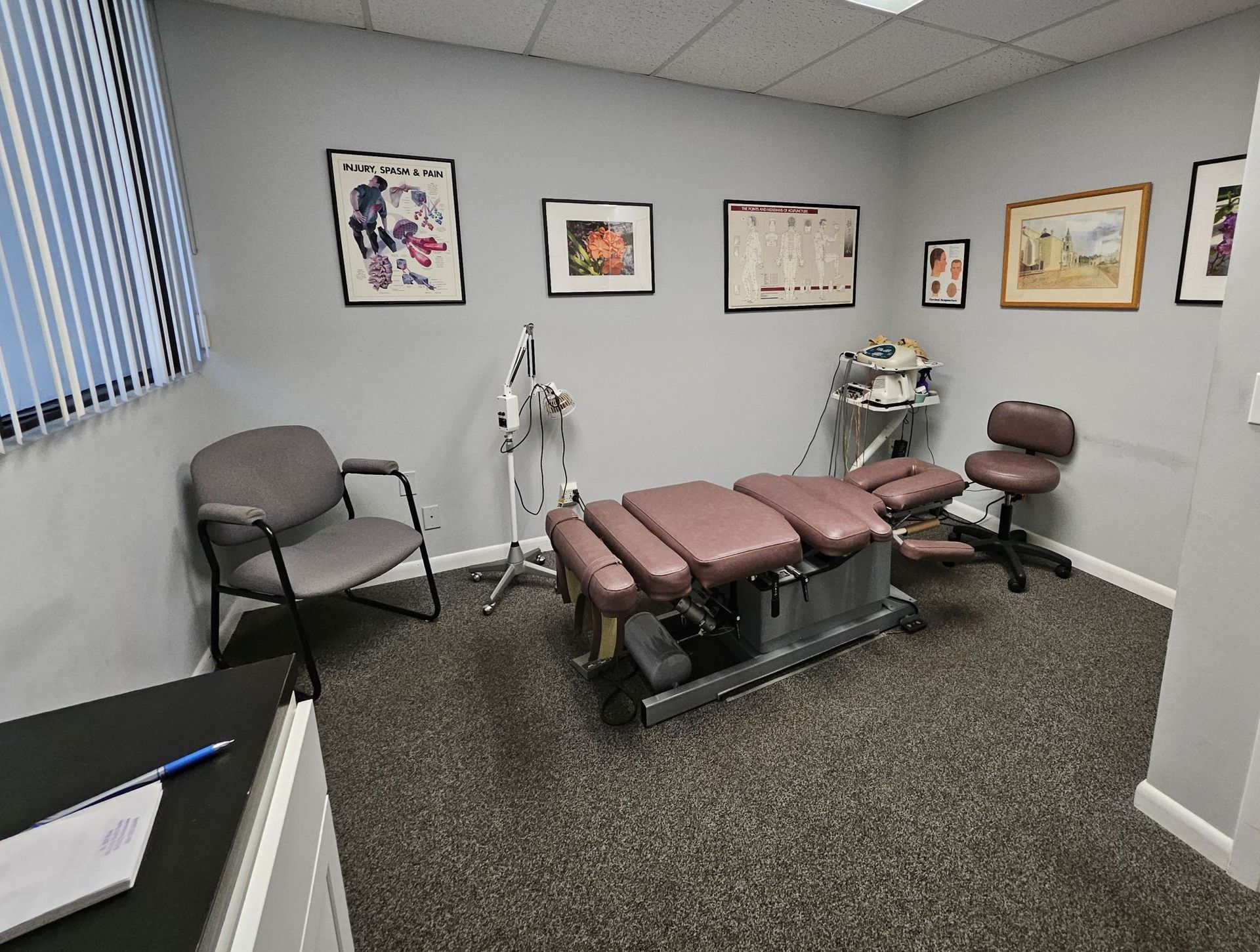 Chiropractic treatment room with exam table, chairs, and framed wall art.