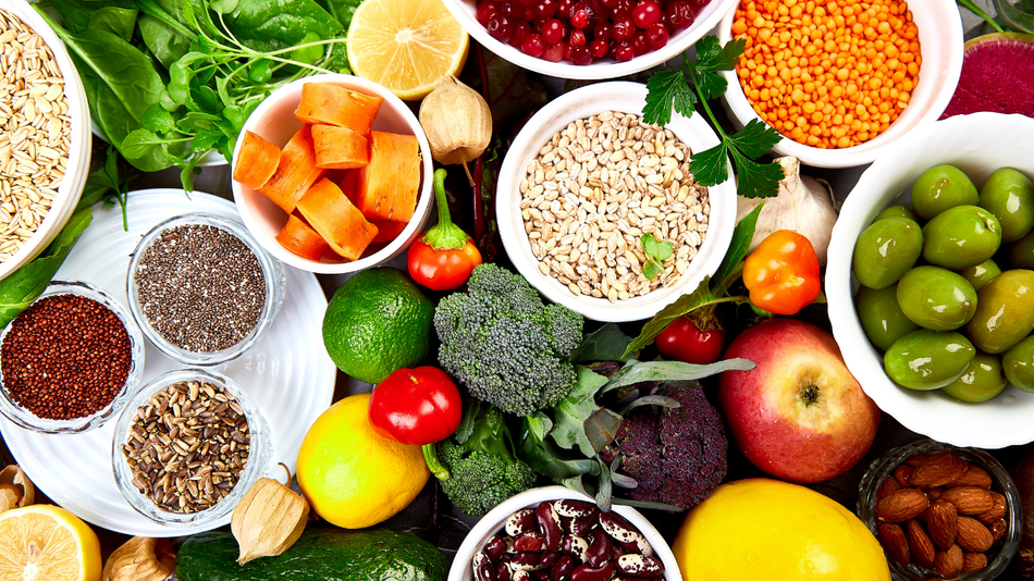 Overhead view of various colorful fresh vegetables, fruits, and grains in white bowls.