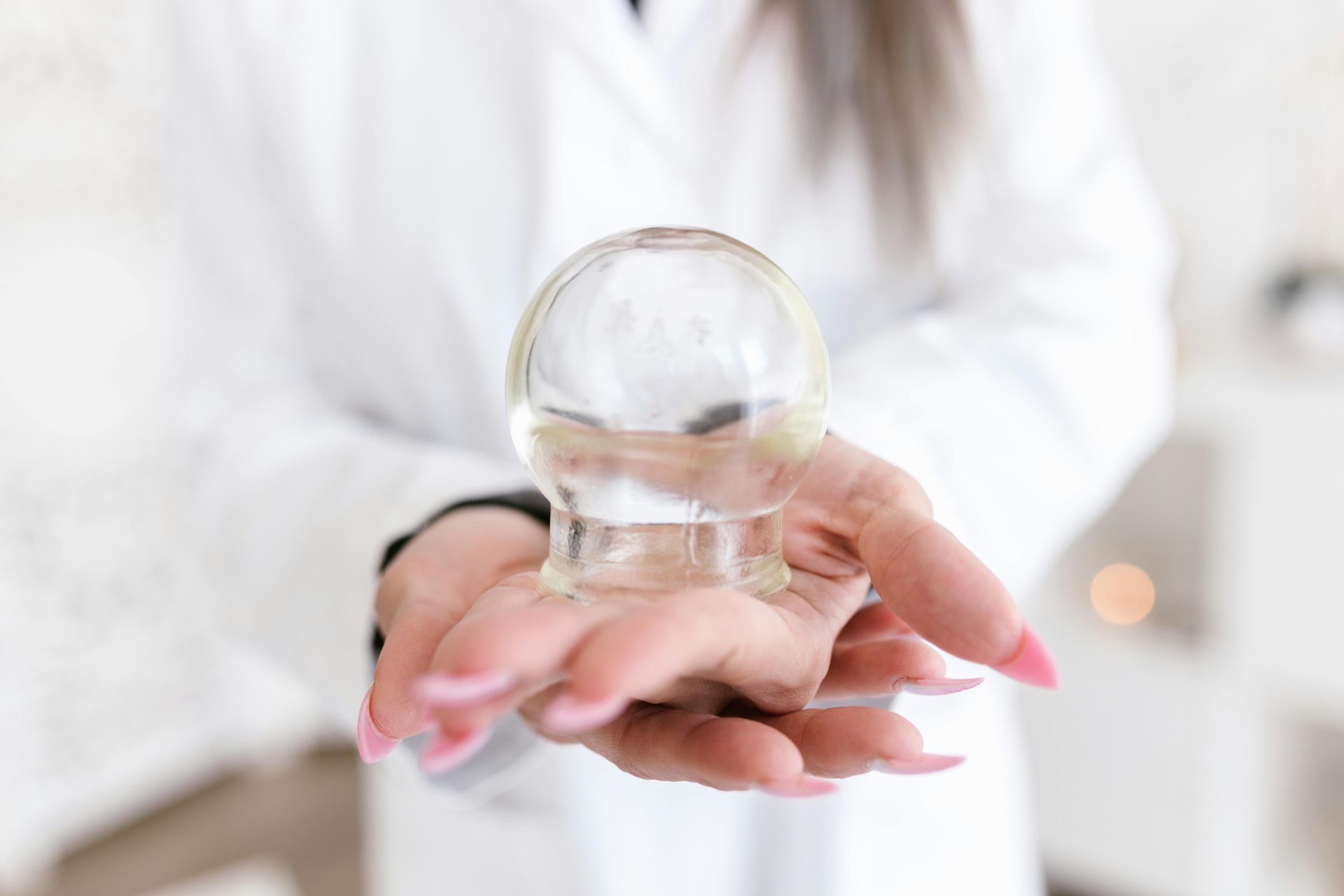A hand holding a clear crystal ball, with a white blurred background