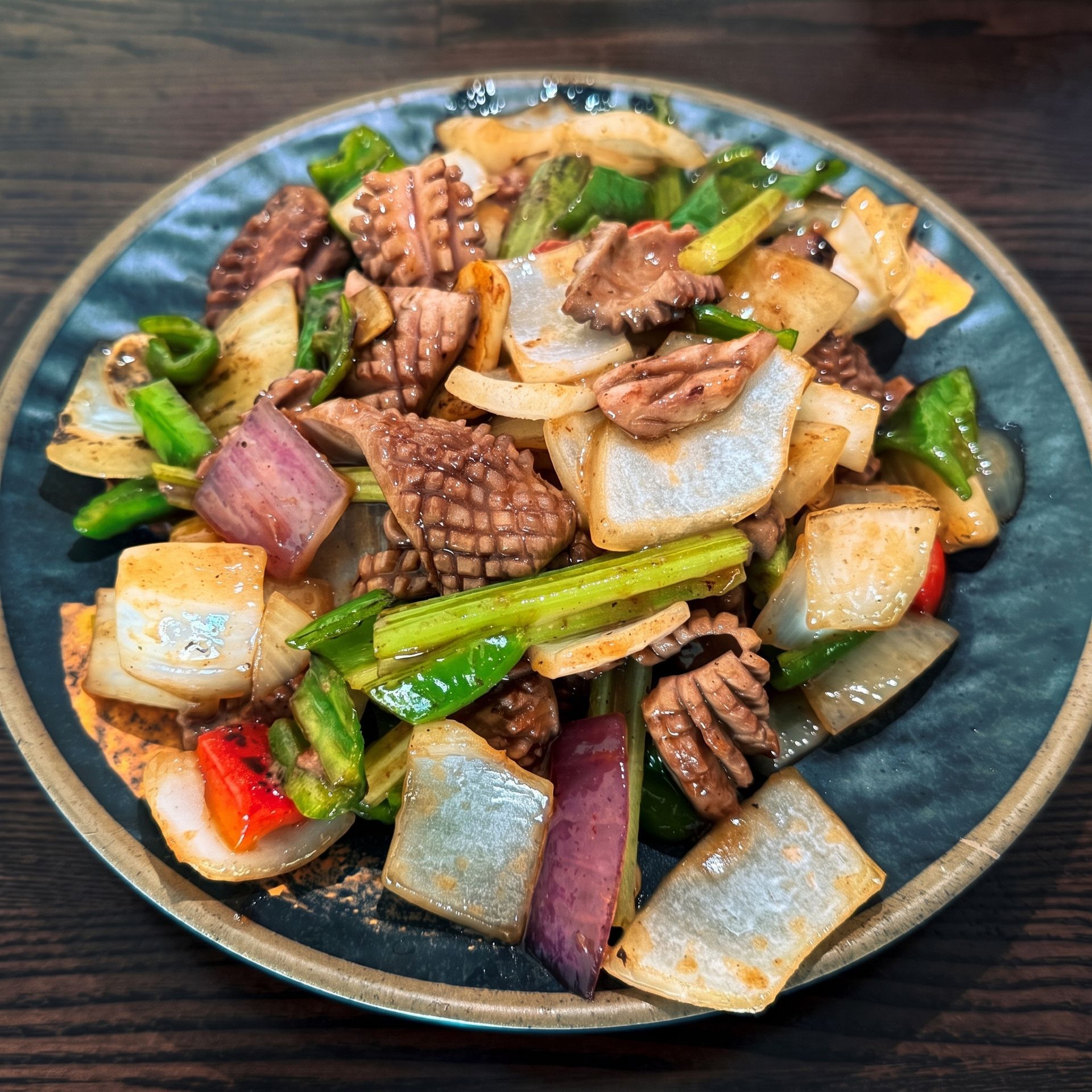 Stir-fried vegetables and meat on a dark plate, with green peppers, onions, and golden tofu pieces.