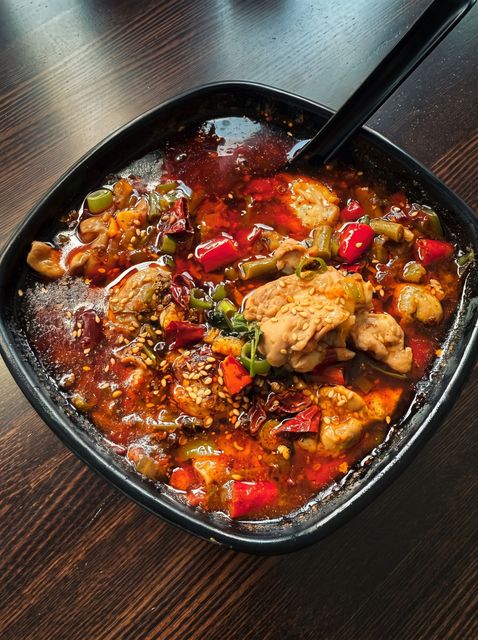 Bowl of spicy stir-fry with red peppers and meat on a dark table