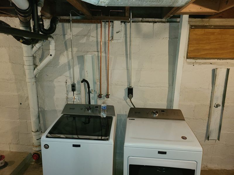Laundry room with a washing machine and dryer beneath exposed pipes and utility connections