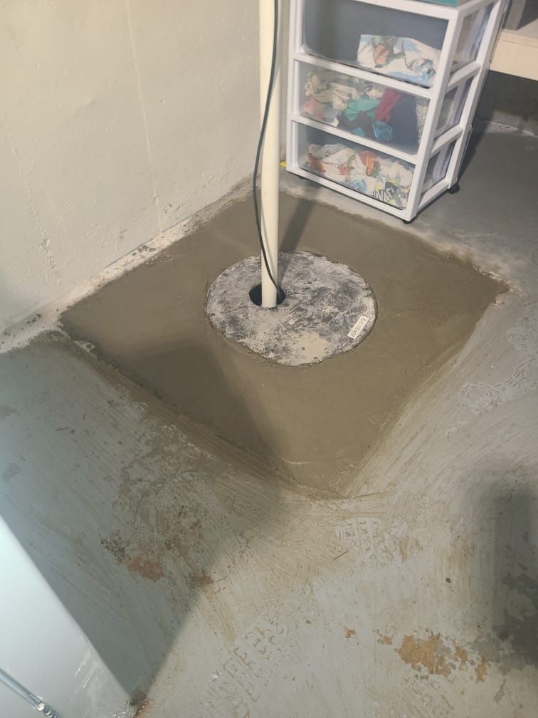 Basement floor with a concrete patch around a pole and a small plastic drawer unit nearby