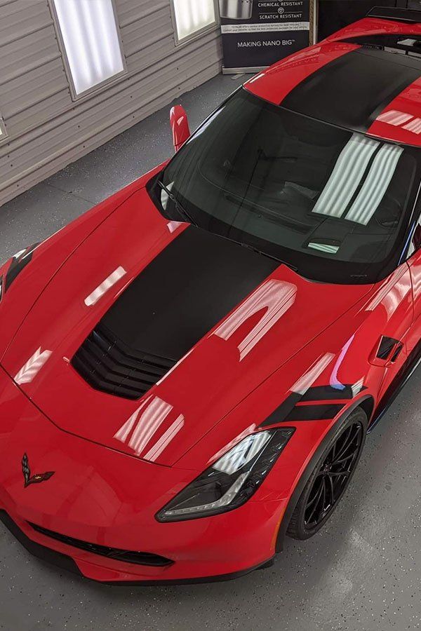 A red corvette with black stripes on the hood is parked in a garage.