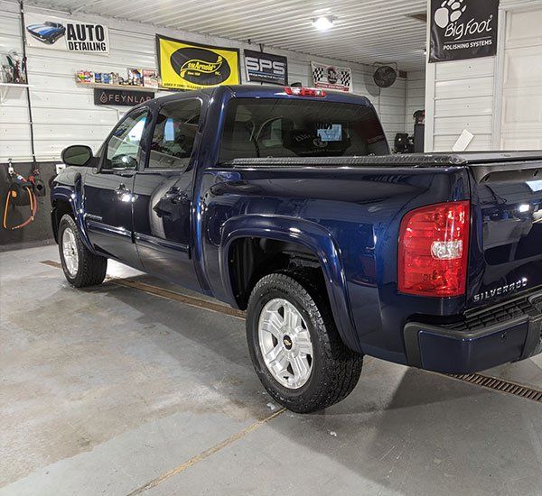 A blue pickup truck is parked in a garage for detailing