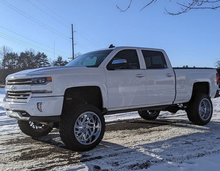 A white truck is parked in the snow on a snowy road.