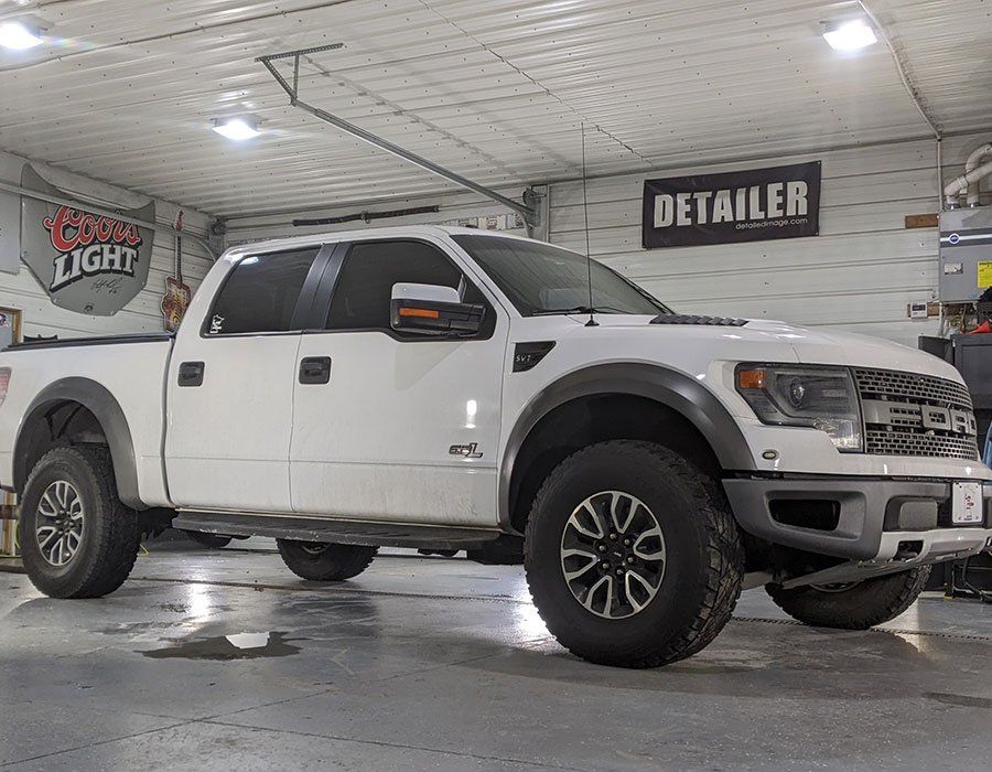 A white truck is parked in a garage next to a sign that says detailer.