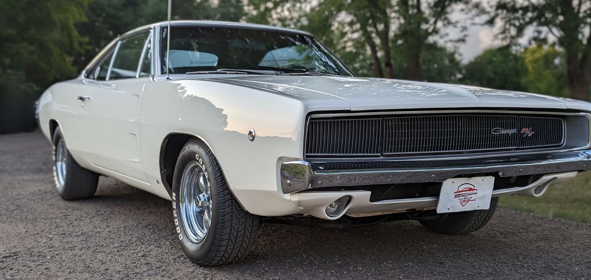A white dodge charger is parked on a gravel road