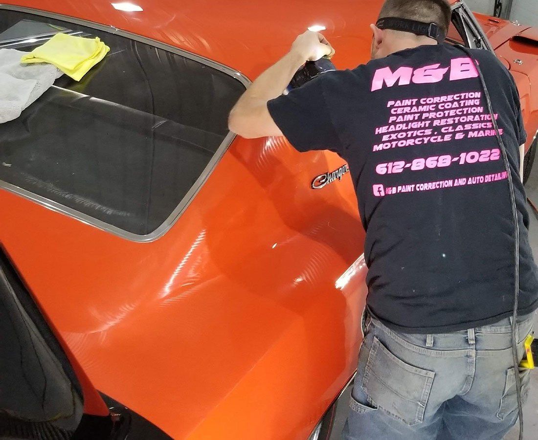 A man wearing a shirt that says mgb is working on an orange car