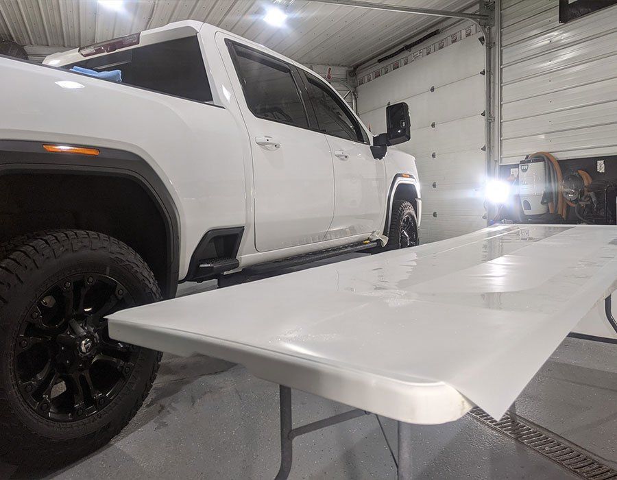 A white truck is parked next to a white table in a garage.