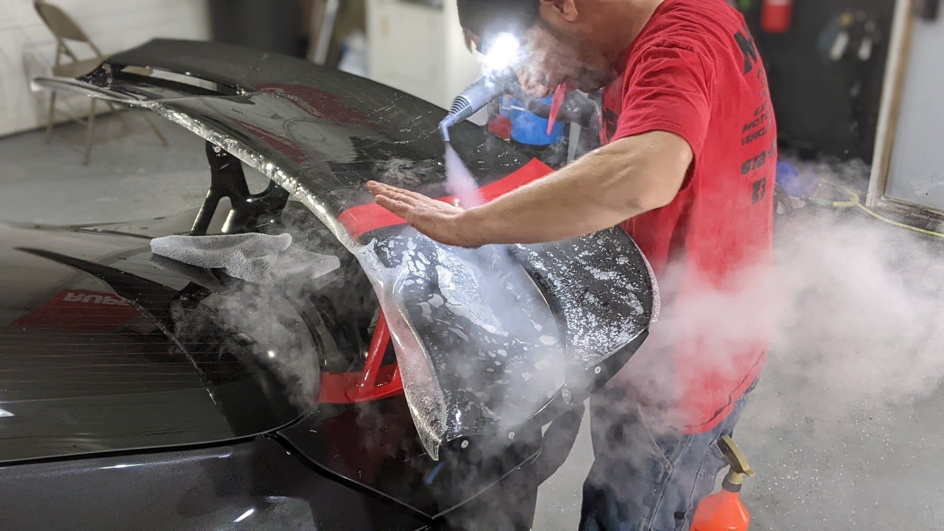 A man in a red shirt is cleaning the hood of a car.