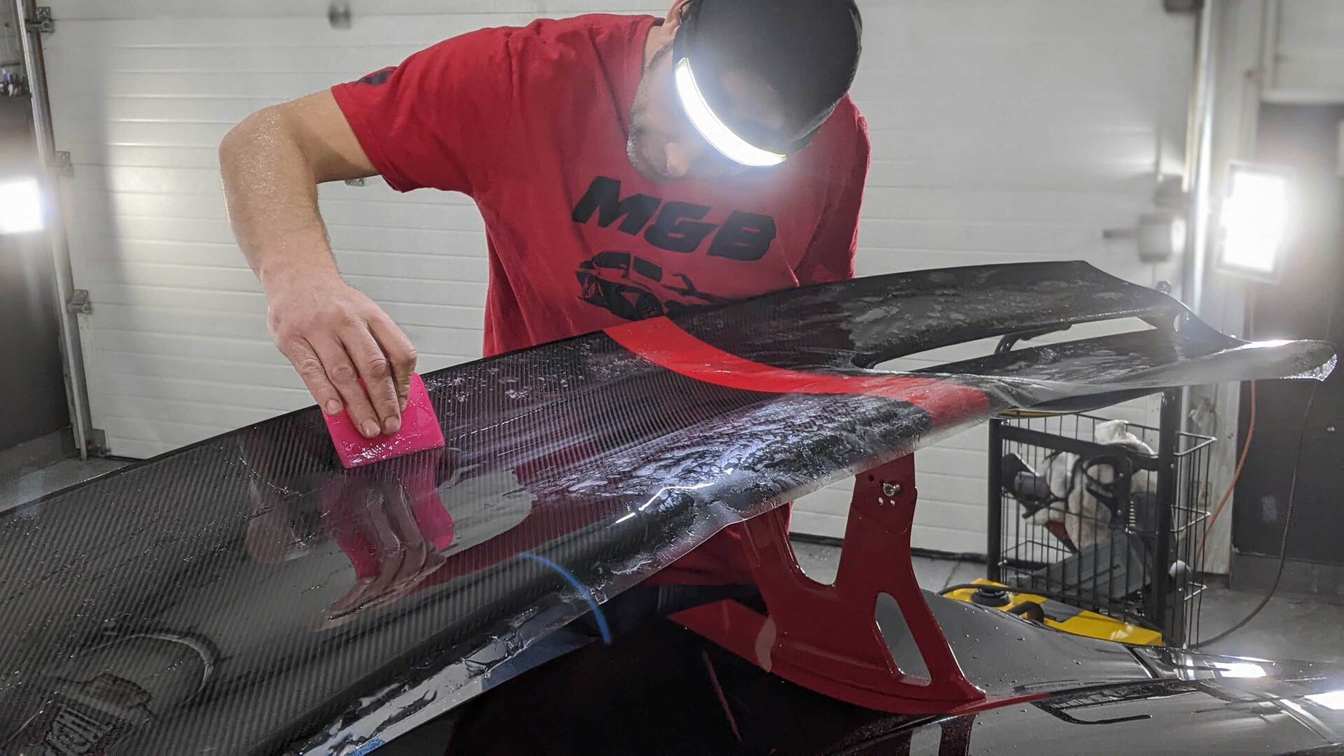 A man in a red shirt is working on a car in a garage.