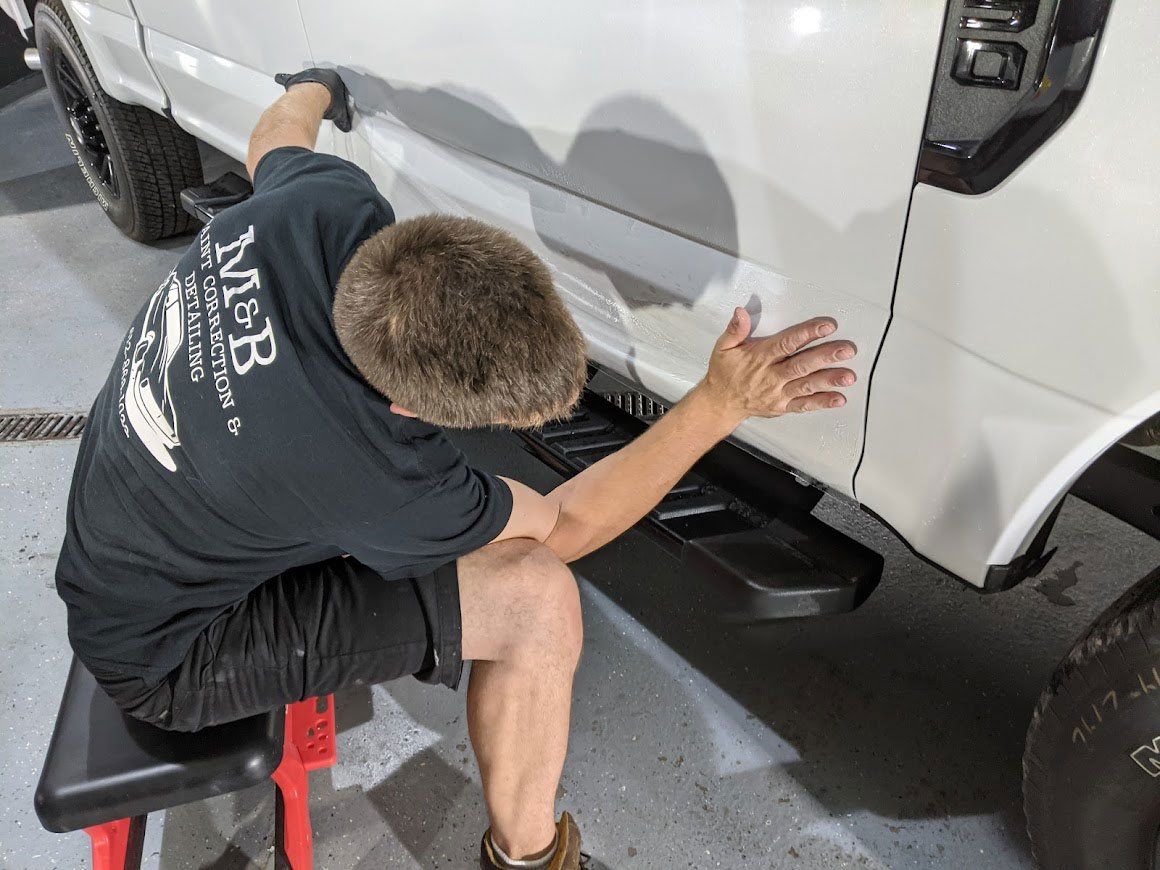 A man is kneeling down next to a white truck in a garage.