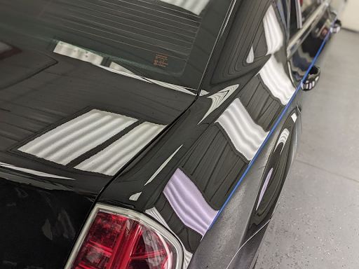 Black car with a glossy finish reflects the ceiling lights. The rear light is visible.
