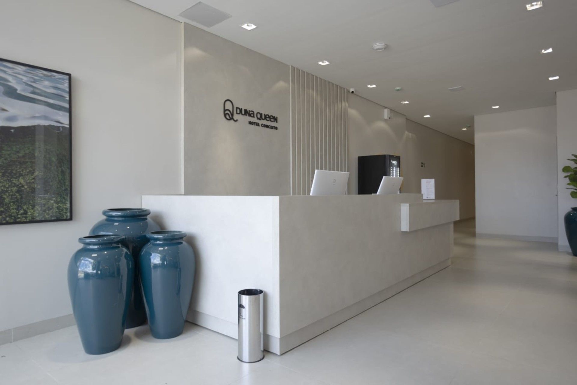 Área de recepção com balcão bege, obras de arte com temática praiana e estação de café.