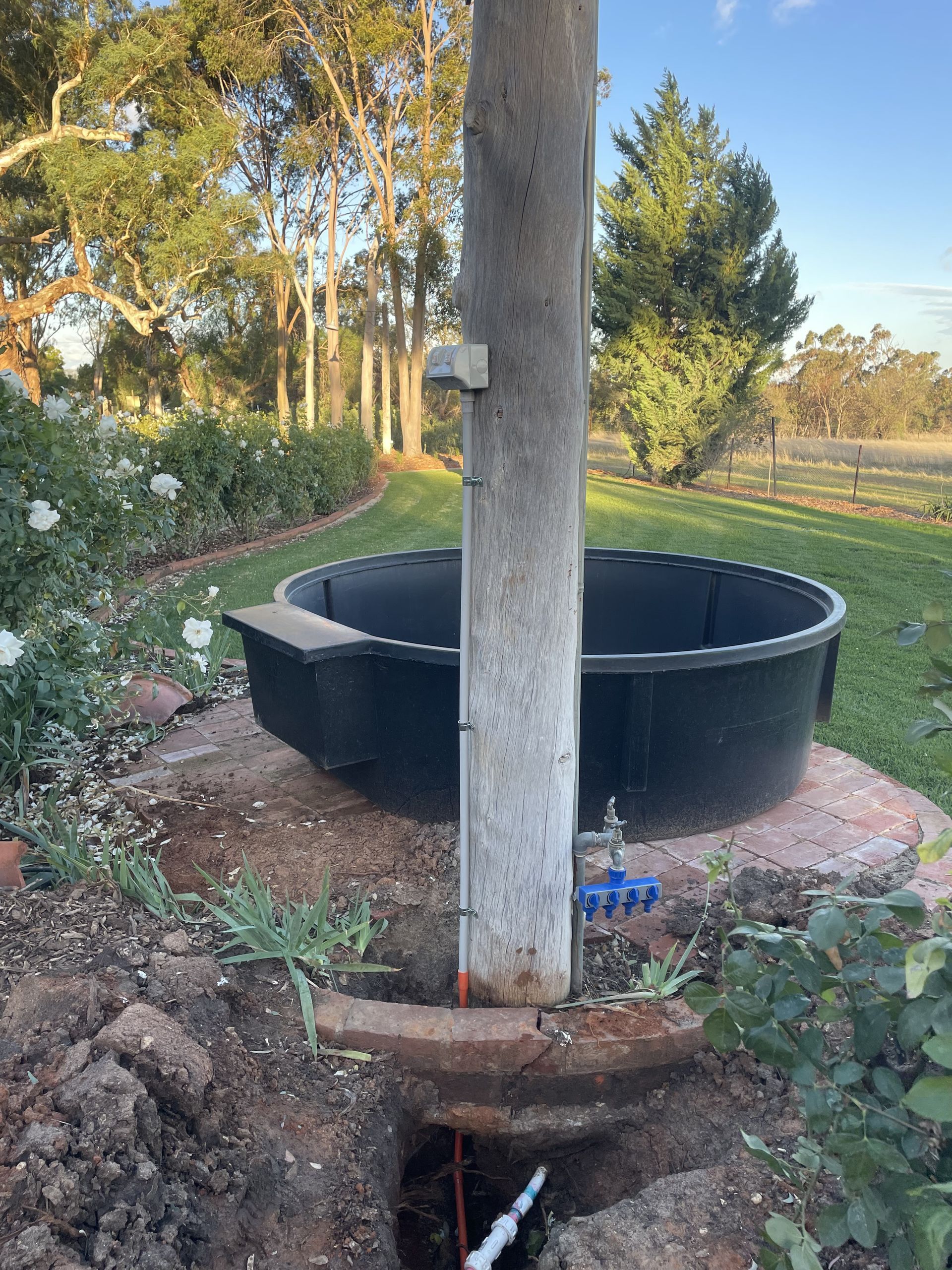 Black circular tank in a garden beside a concrete utility pole and exposed trench. — Craig Stewart Electrical in East Wagga Wagga, NSW