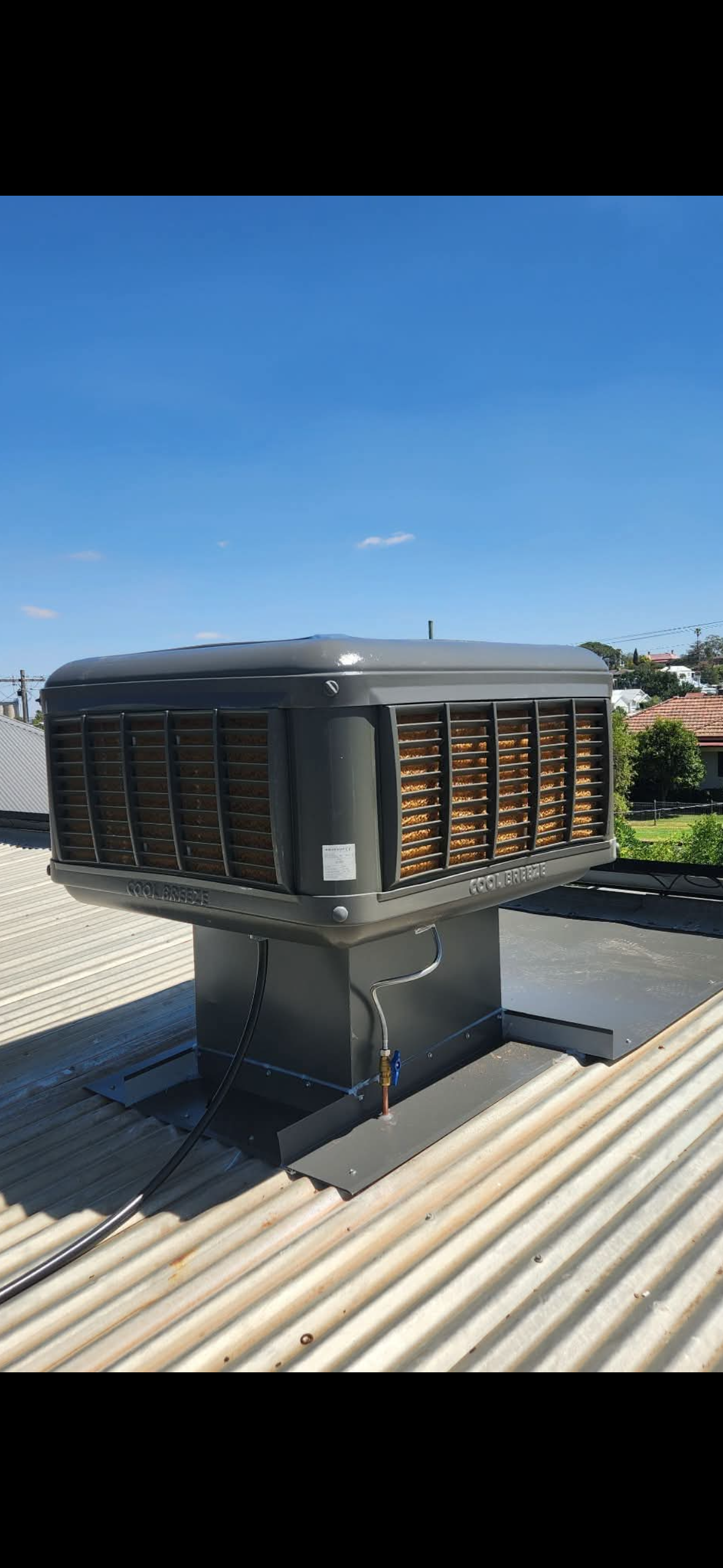 Black rooftop HVAC unit on a corrugated metal roof under a clear blue sky — Craig Stewart Electrical in East Wagga Wagga, NSW