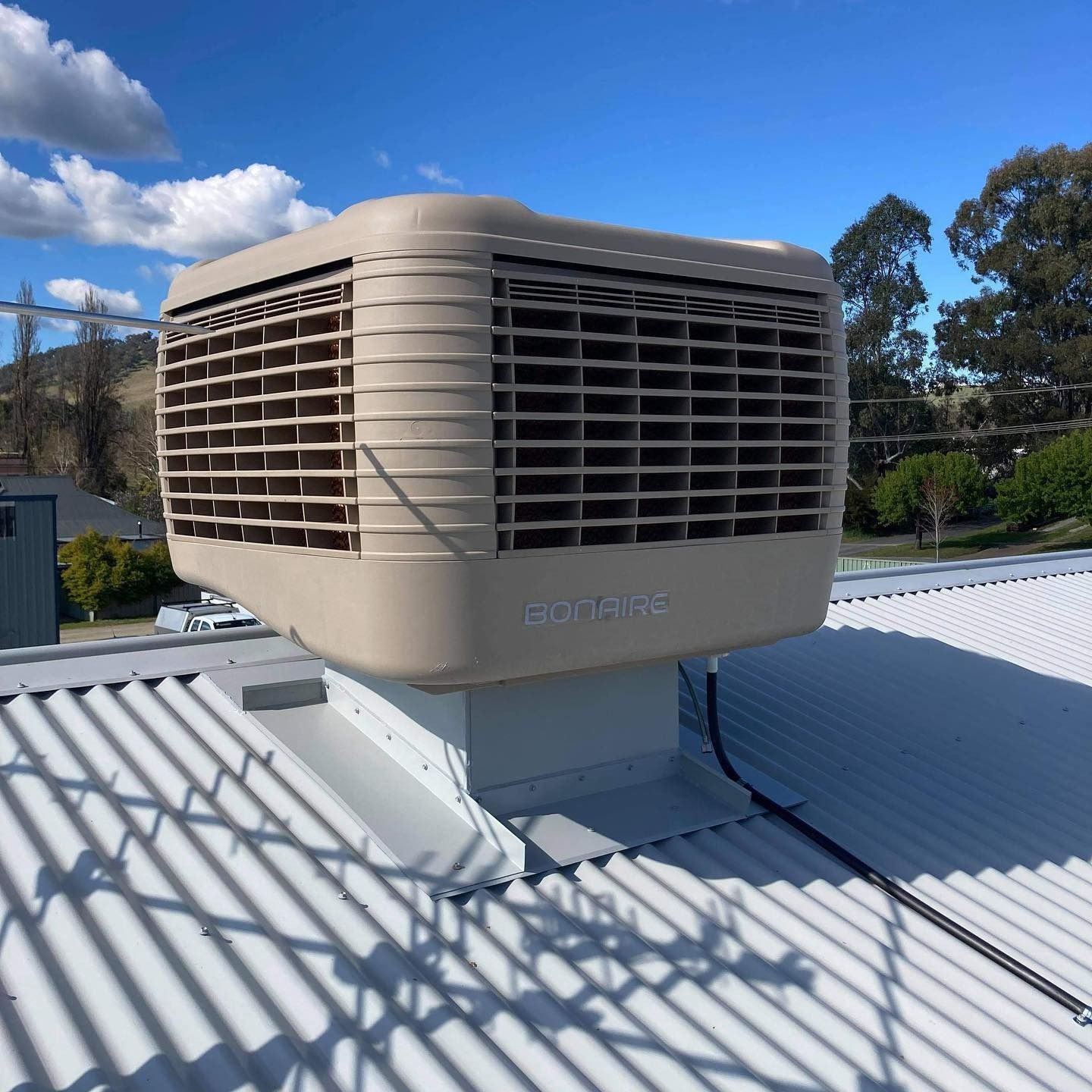 Beige rooftop evaporative cooler on a corrugated metal roof under a blue sky with clouds — Craig Stewart Electrical in East Wagga Wagga, NSW