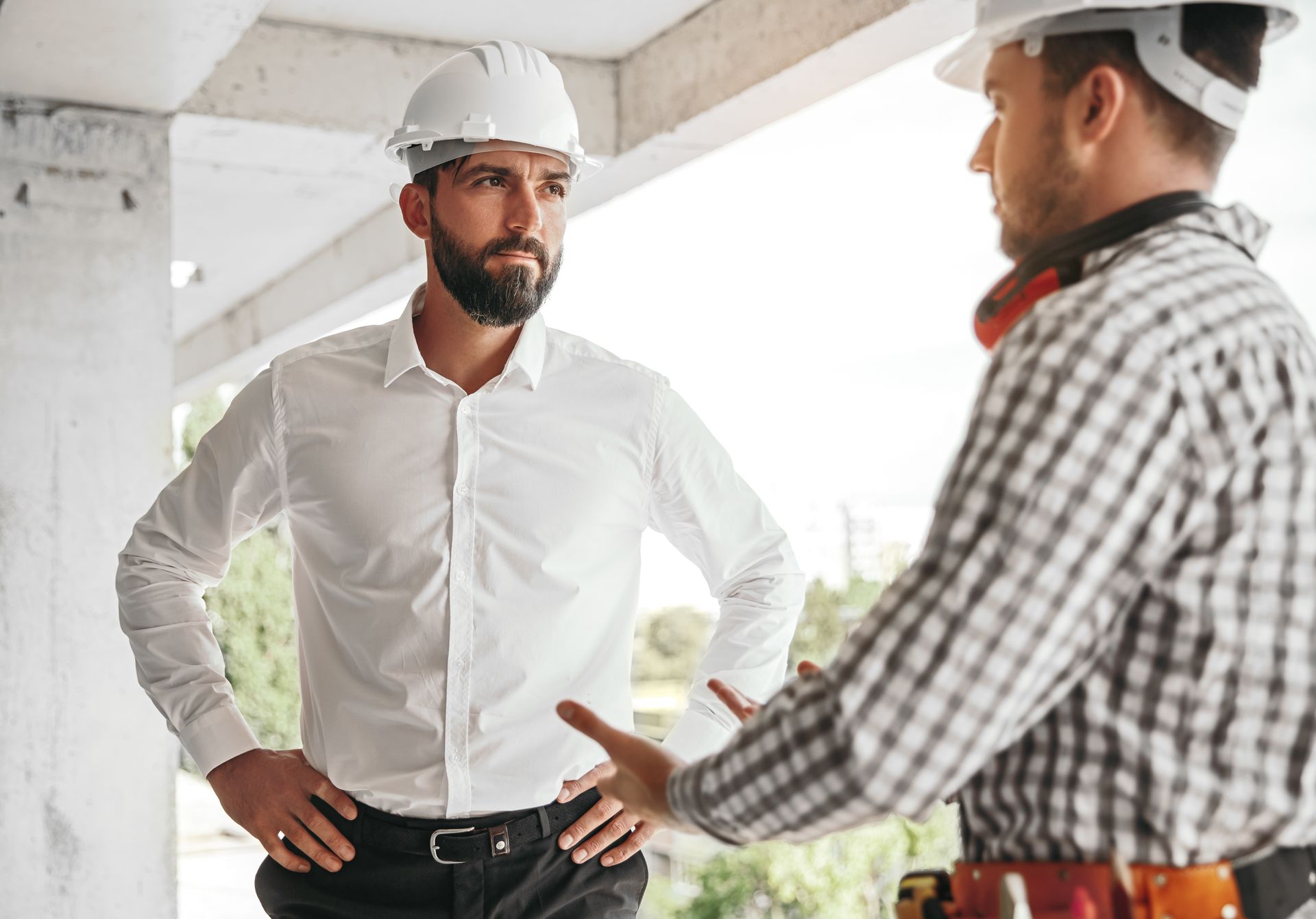 Two construction workers in hard hats discussing plans at a building site