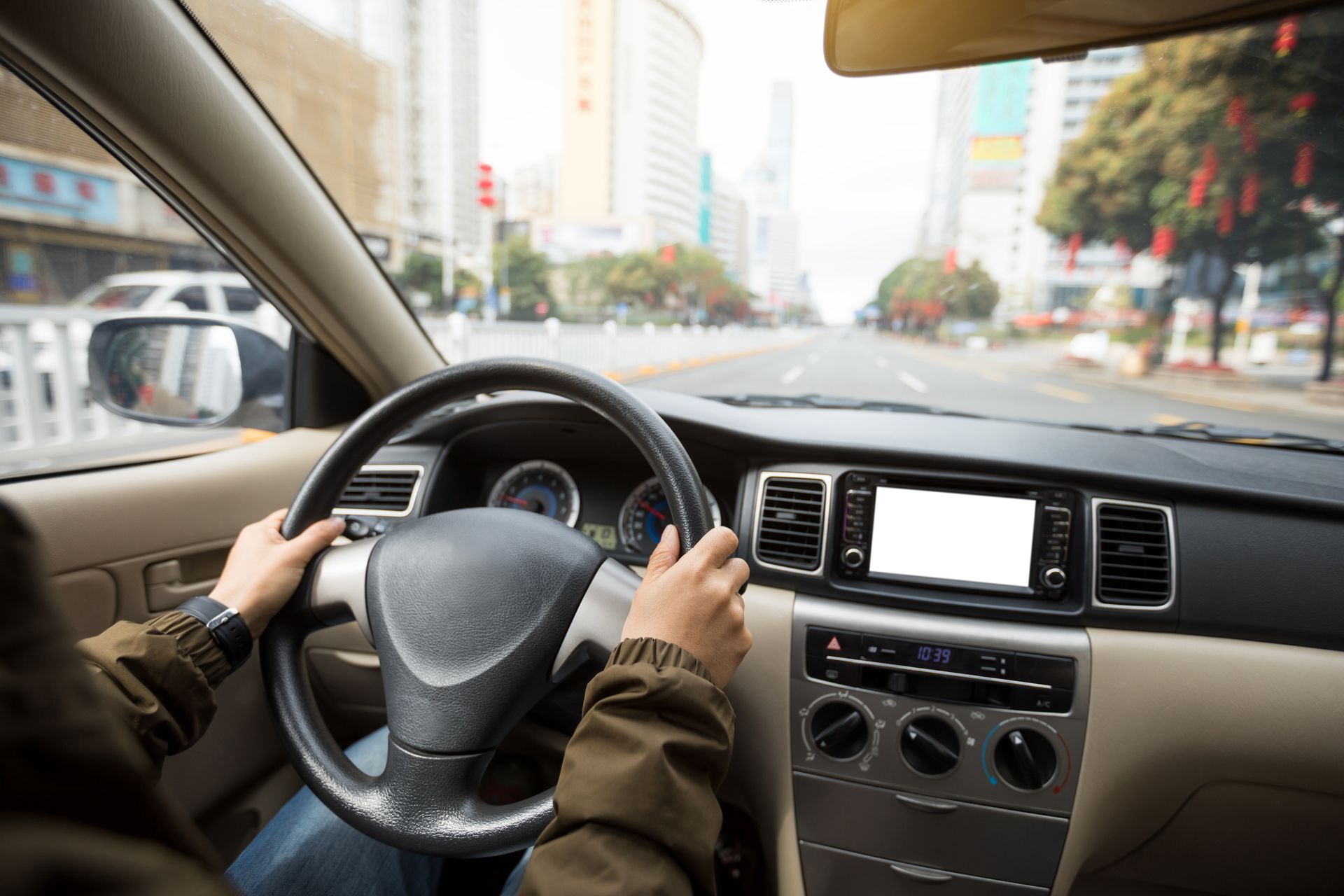 Driver holding steering wheel inside a car on a city street, with dashboard and center console visible